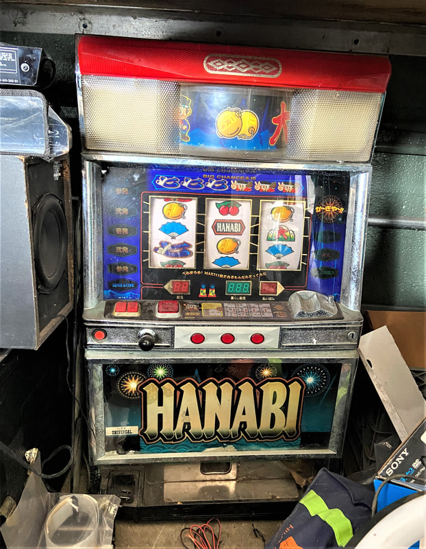 A Japanese Hanabi slot machine with fireworks icons around the name, and images on the slot wheels of tourquoise fans, a pair of cherries on a stem, and others. 