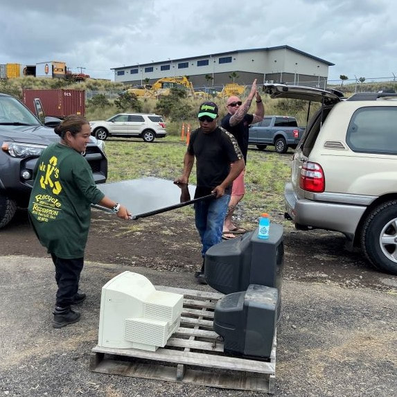Two staffers of Mr. K's unload a flat screen TV from the back of a resident's car and carry it to a pallet, at the Kailua-Kona collection site.